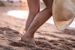 Feet of a woman standing on the beach at sunset with a hat