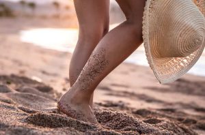 Feet of a woman standing on the beach at sunset with a hat